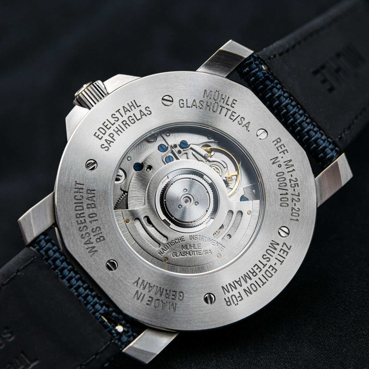 Nahaufnahme des Gehäusebodens der ZEIT-Sonderedition Automatikuhr »29er« Casual (2026) von Mühle-Glashütte. Sichtboden mit sichtbarem Automatikwerk, gravierte Edelstahlrückseite, schwarzes Armband mit blauer Naht, technische Details und Seriennummer eingraviert.