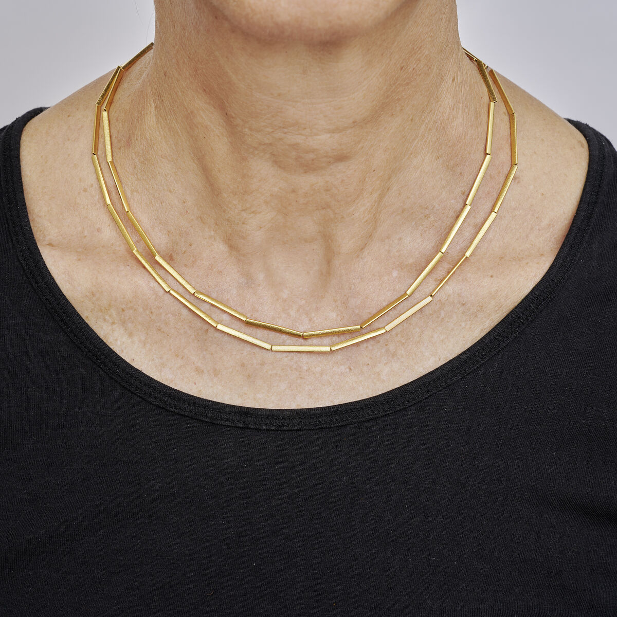 Eine elegante, feingoldplattierte Halmkette aus Silber ist doppelt um den Hals einer Person gelegt. Die Gliederkette hat eine moderne, minimalistische Optik und wird zu einem schlichten schwarzen Oberteil getragen.