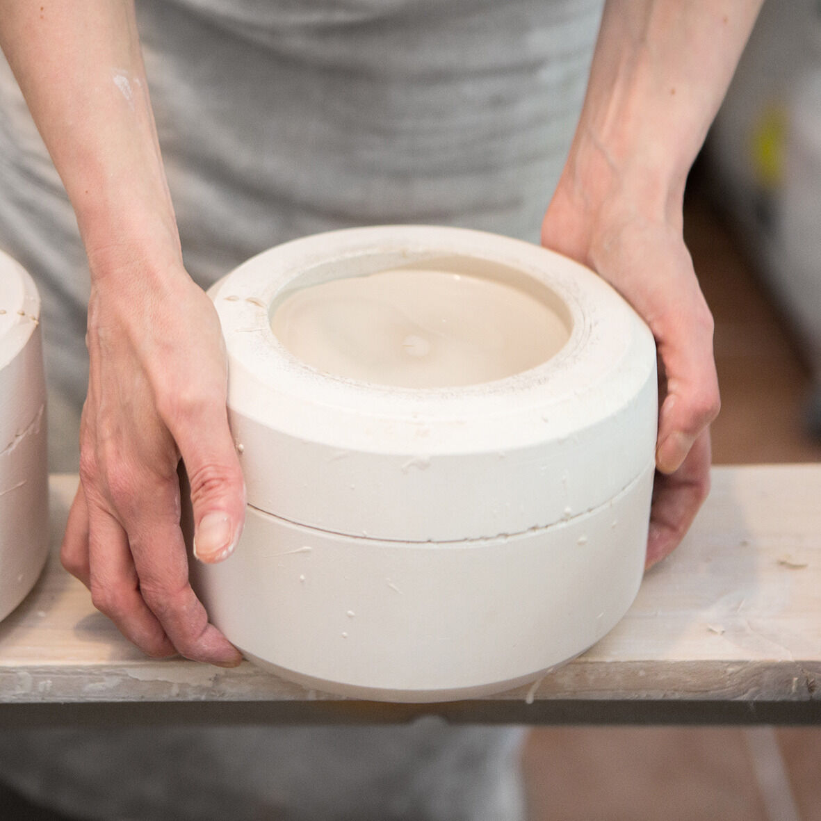 Eine Person bearbeitet einen Kerzenhalter aus Porzellan in einer Manufaktur. Der Kerzenhalter ist in einem minimalistischen Design gehalten und wird kunsthandwerklich gefertigt.