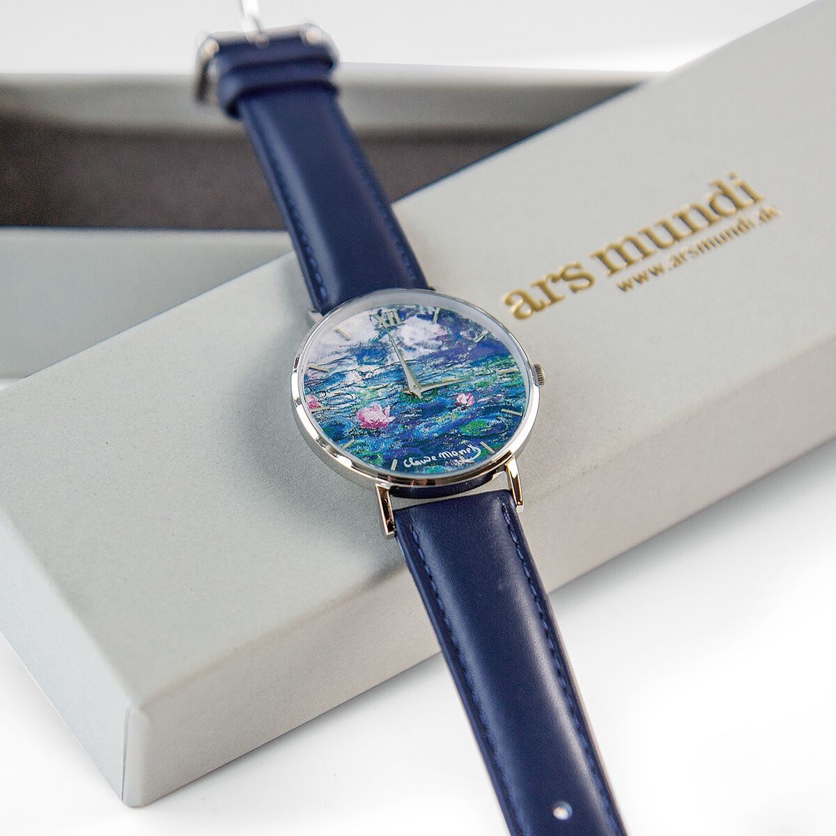 Künstler-Armbanduhr »Monet - Les Nymphéas« mit einem Zifferblatt, das Monets Seerosenmotiv zeigt. Die Uhr hat ein blaues Armband und wird in einer schicken Verpackung präsentiert.
