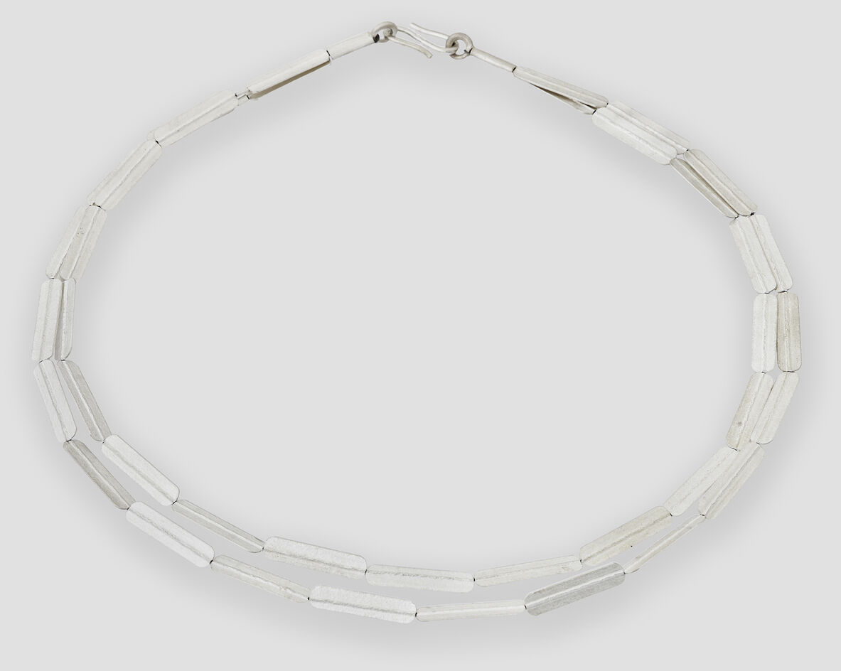 Silbernes Collier mit geprägtem Streifenmuster, bestehend aus rechteckigen, glänzenden Gliedern, auf einem neutralen hellgrauen Hintergrund, geeignet als elegantes Schmuckstück für verschiedene festliche Anlässe.
