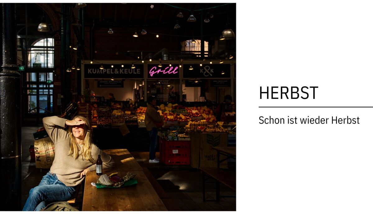 Eine Frau sitzt an einem Holztisch in einem Marktgebäude. Im Hintergrund sieht man einen Marktstand mit einer Neonreklame 'grill'. Text auf der rechten Seite: 'HERBST Schon ist wieder Herbst'.