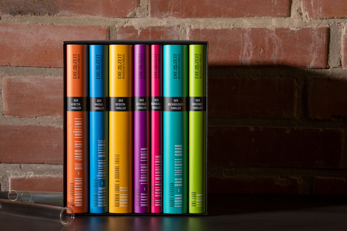 Ein Foto der ZEIT-Edition »Wissenschafts-Thriller« zeigt eine Sammlung von sieben farbenfrohen Büchern in einem schwarzen Bücherregal, das vor einer Wand mit roten Backsteinen steht. Die Bücher sind in den Farben rot, orange, gelb, blau, hellblau, grün und pink.