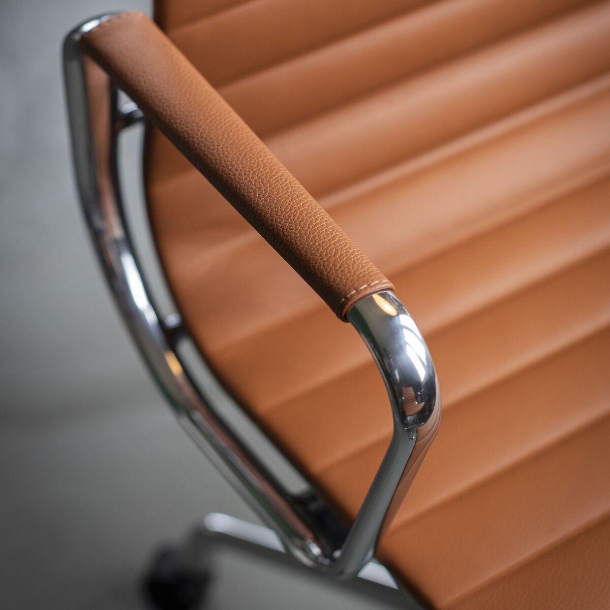 Nahaufnahme eines polierten Vitra Alu Chair EA 118. Der Stuhl hat eine braune Lederpolsterung und glänzende Metallarmlehnen. Das Design ist modern und minimalistisch.