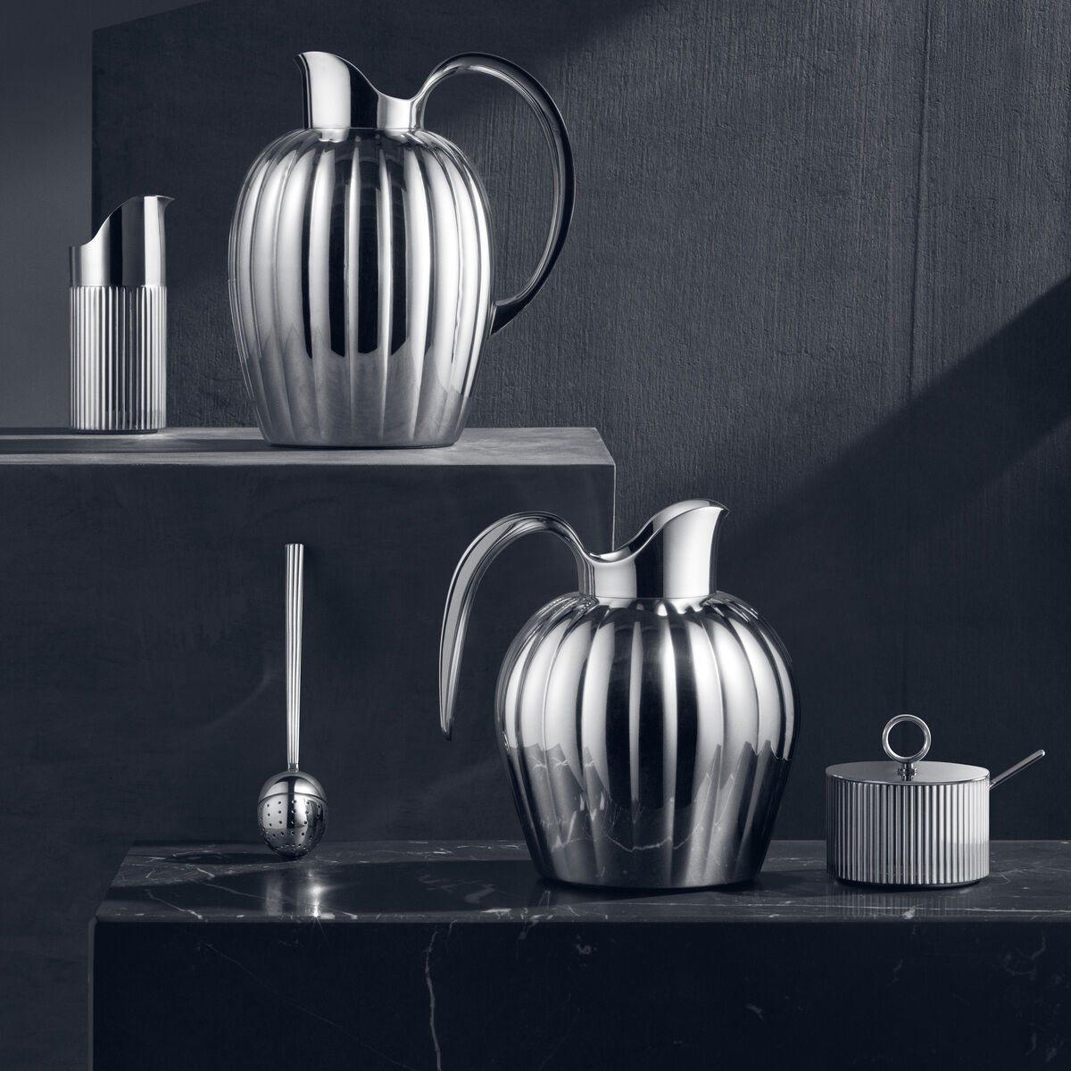 Ein Setting aus silbernem und minimalistischen Accessoires, darunter eine Zuckerdose mit einem Löffel, die in einem klassischen und eleganten Stil gestaltet sind.