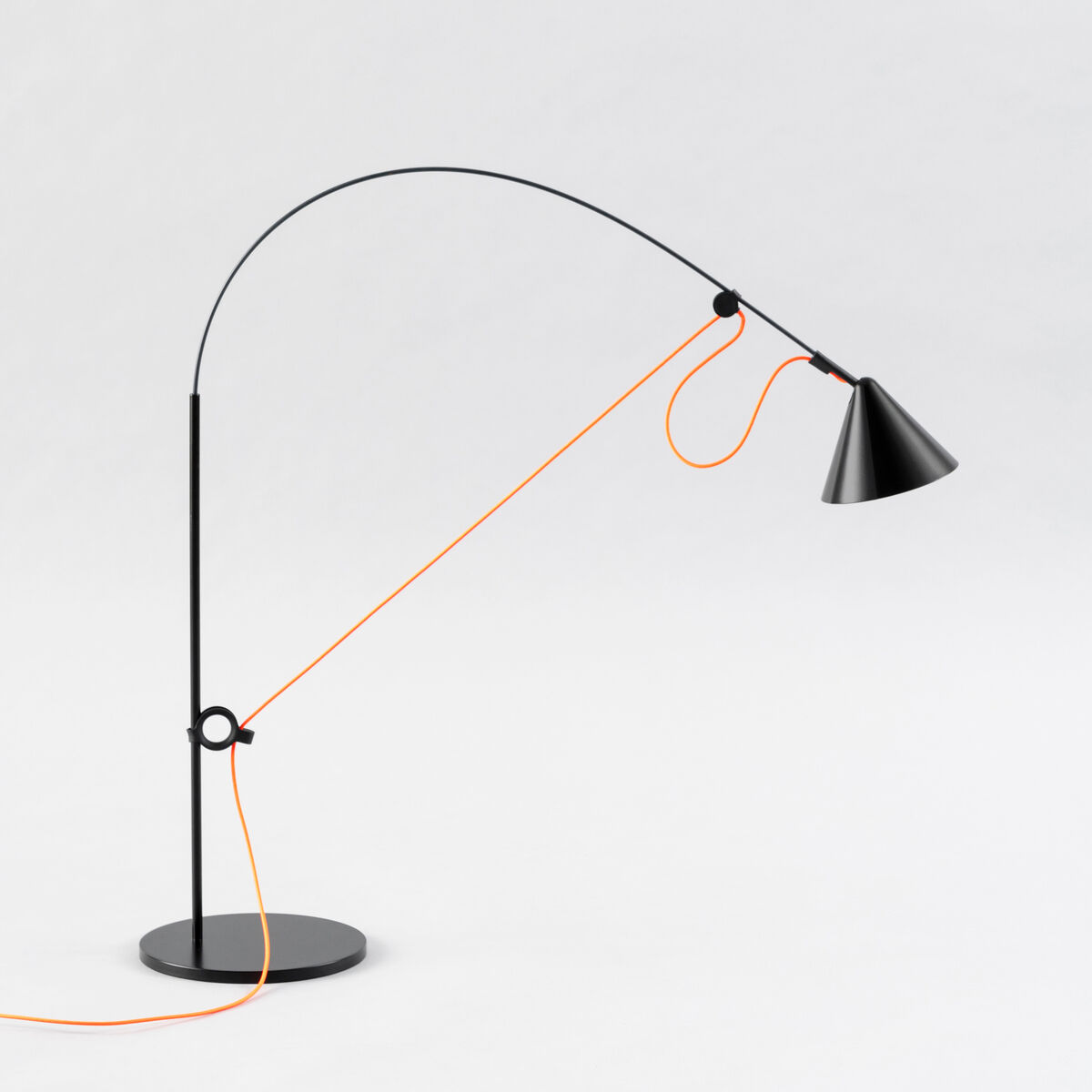 Eine moderne Tischlampe namens 'AYNO' mit einem schwarzen, verstellbaren Arm und einem orangefarbenen Kabel, das um die Lampe gewickelt ist. Die Lampe hat eine konische Form und steht auf einem runden Fuß.