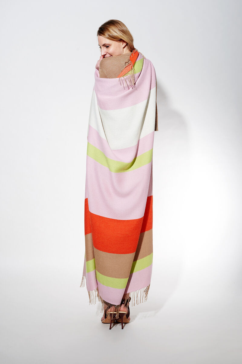 Frau trägt ein Cape aus Alpaka-Wolle mit Streifen in Rosa, Weiß, Grün, Orange und Beige.