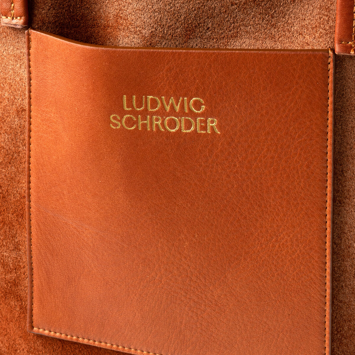 Eine Nahaufnahme der Ledershopper-Tasche »Marie« in Braun mit goldener Schrift 'Ludwig Schröder' auf der Vorderseite. Die Tasche zeigt hochwertige Handwerkskunst und elegantes Design.