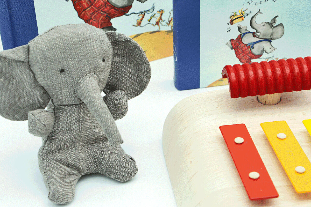 Ein Geschenkset bestehend aus einem grauen Plüschelefanten, einem Xylophon mit roten, gelben und weißen Elementen sowie einem Kinderbuch mit bunten Illustrationen. Ideal für Kinder zur frühkindlichen musikalischen Bildung.