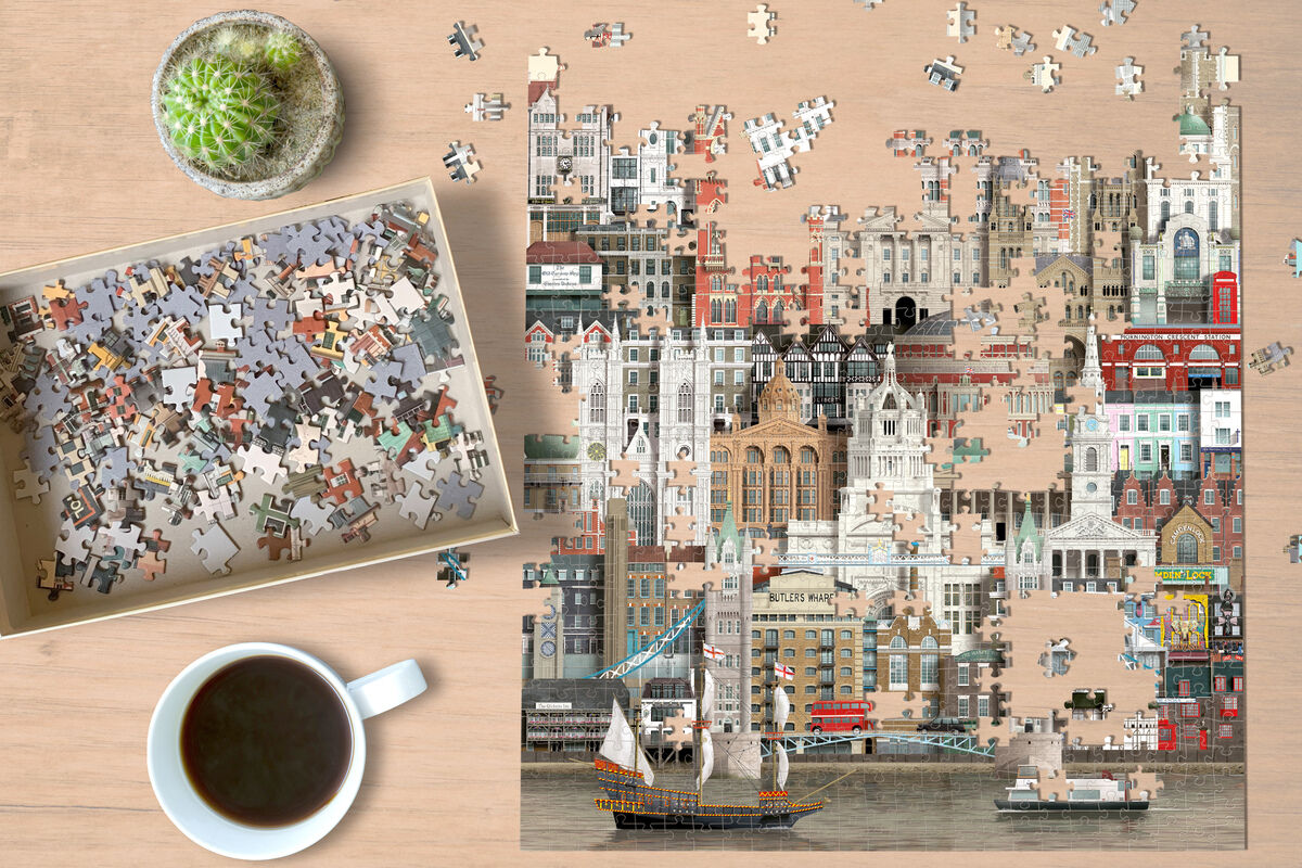 Ein Puzzle mit 1000 Teilen zeigt die Skyline von London mit verschiedenen Wahrzeichen. Ein teilweise fertiggestelltes Puzzle liegt auf einem Holztisch neben einer Tasse Kaffee und einem kleinen Pflanzentopf.