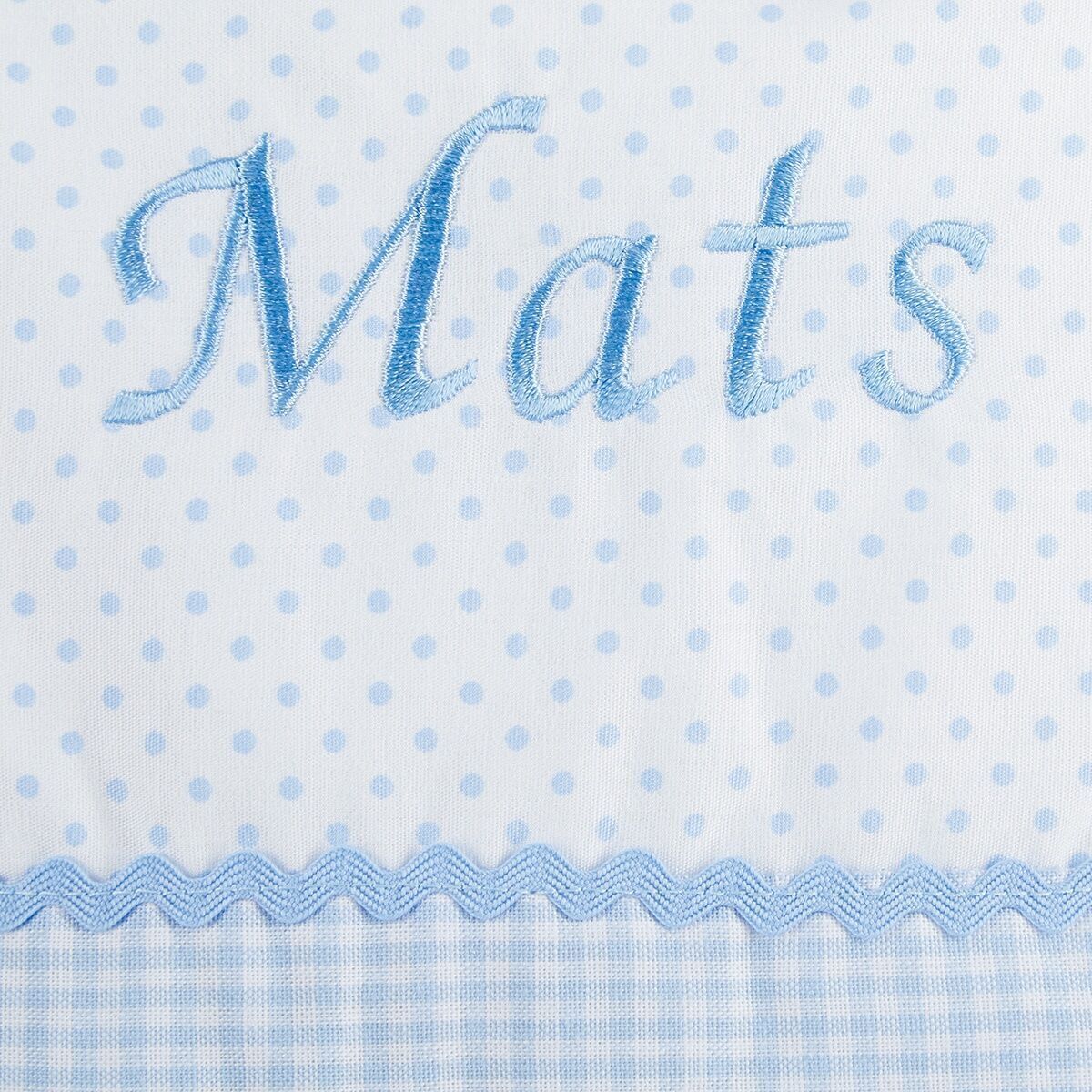 Nahaufnahme eines personalisierten Namenskissens mit dem aufgestickten Namen "Mats" in blau. Der Stoff ist weiß mit blauen Polka Dots und einem blauen Vichy-Karo Muster.