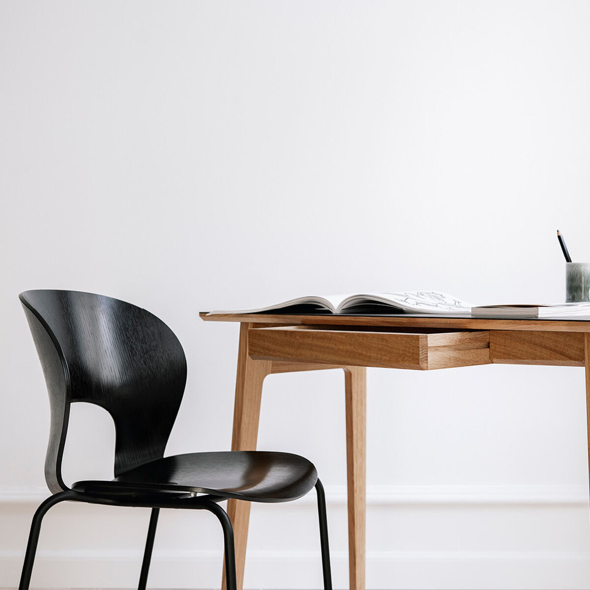 Moderner, schwarz gefärbter Esszimmerstuhl aus Holz, der neben einem schlichten Holztisch mit einigen Dekorationsgegenständen in einem hellen Raum steht.