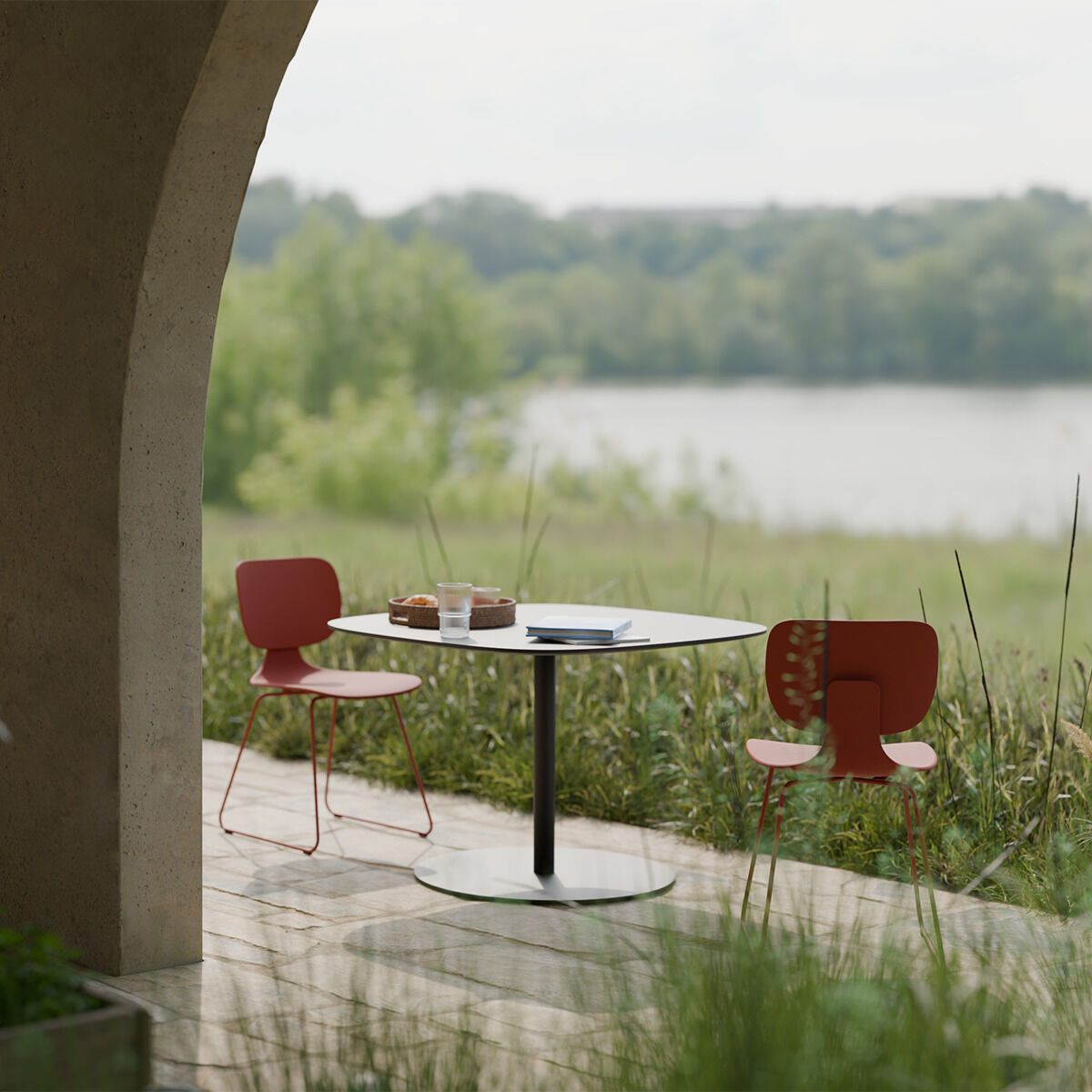 Zwei rote Stühle und ein runder Tisch stehen auf einer Terrasse mit Blick auf eine grasbewachsene Landschaft und einen See, unter einem Torbogen im Freien.