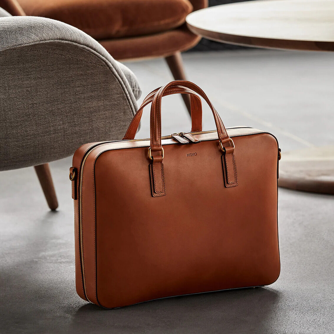 Businesstasche 'MORRIS' in naturbrauner Farbe mit zwei Griffen und Reißverschluss auf einem modernen Interieur-Hintergrund.