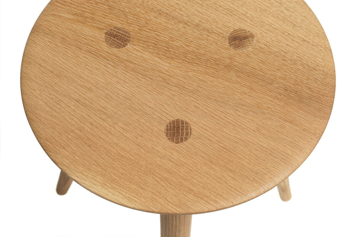Ein runder Holzschemel namens »Heidi« aus naturfarbenem Holz mit drei Punkten auf der Sitzfläche. Der Hocker steht auf vier stabilen Beinen und hat eine rustikale Optik.
