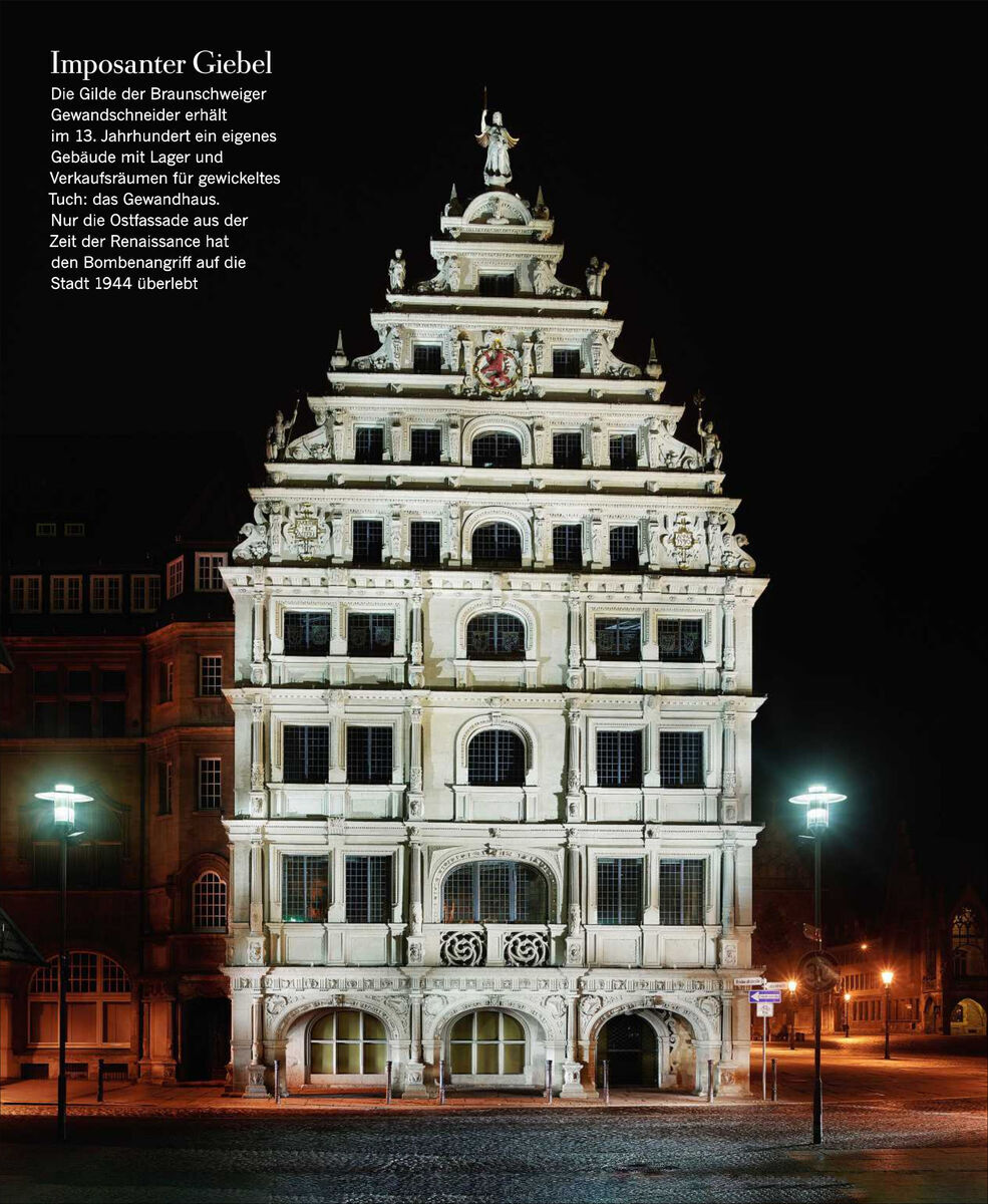 Ein historisches Gebäude mit reich verzierter Fassade bei Nacht beleuchtet. Der Text auf dem Bild beschreibt die Handwerks- und Kaufmannsgilden in Braunschweig im Mittelalter und ihre Bedeutung für die Regionalgeschichte.