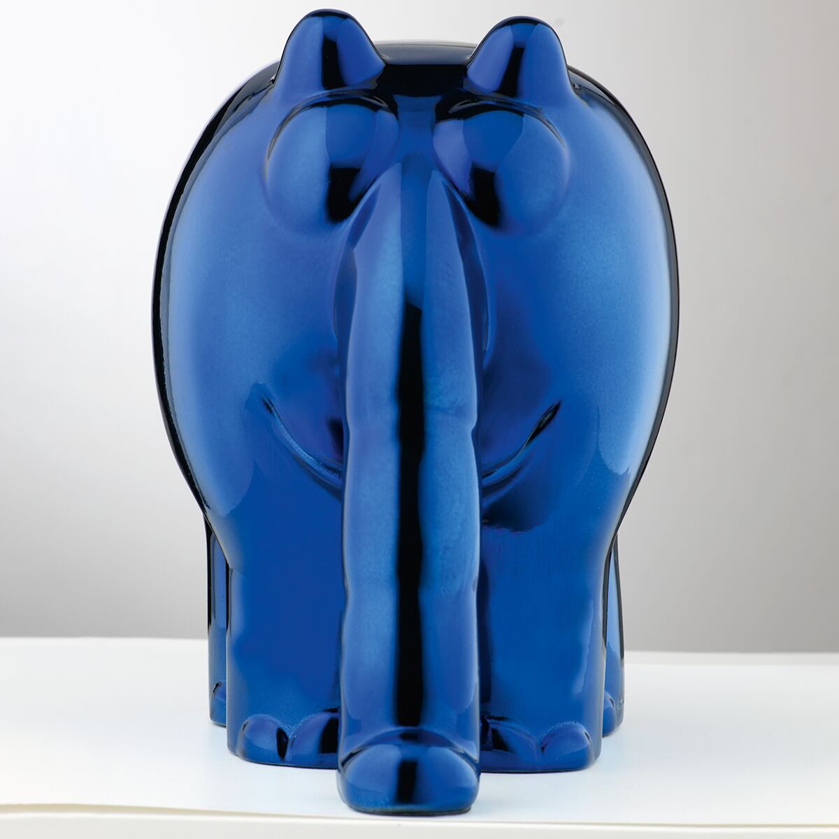 Eine Skulptur des Ottifanten von Otto Waalkes in einer hochglänzenden metallic-blauen Oberfläche. Die Figur steht auf einem hellen Untergrund vor neutralem Hintergrund. Der Ottifant ist von hinten zu sehen, mit dickem Rüssel und rundlichen Formen.