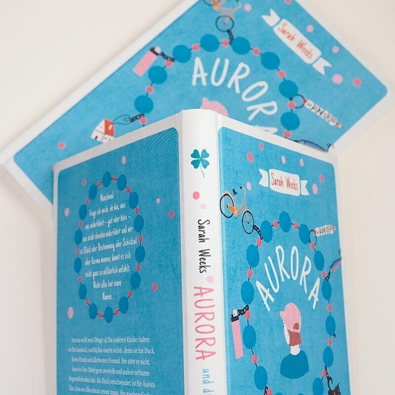 Das Bild zeigt das Buch 'Aurora und die Sache mit dem Glück' von Sarah Weeks. Das Cover ist größtenteils blau mit weißen und rosa Akzenten. Der Titel ist in großen weißen Buchstaben verfasst, umgeben von Illustrationen wie Fahrräder, Bäume und kleine, pinke Vögel.
