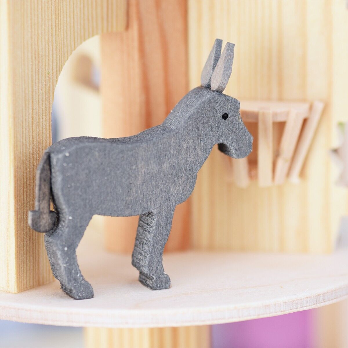 Detailfoto einer hölzernen Weihnachtskrippe in Pyramidenform mit der Figur eines Esels. Das Holz hat eine natürliche Farbe, und der Esel ist grau.