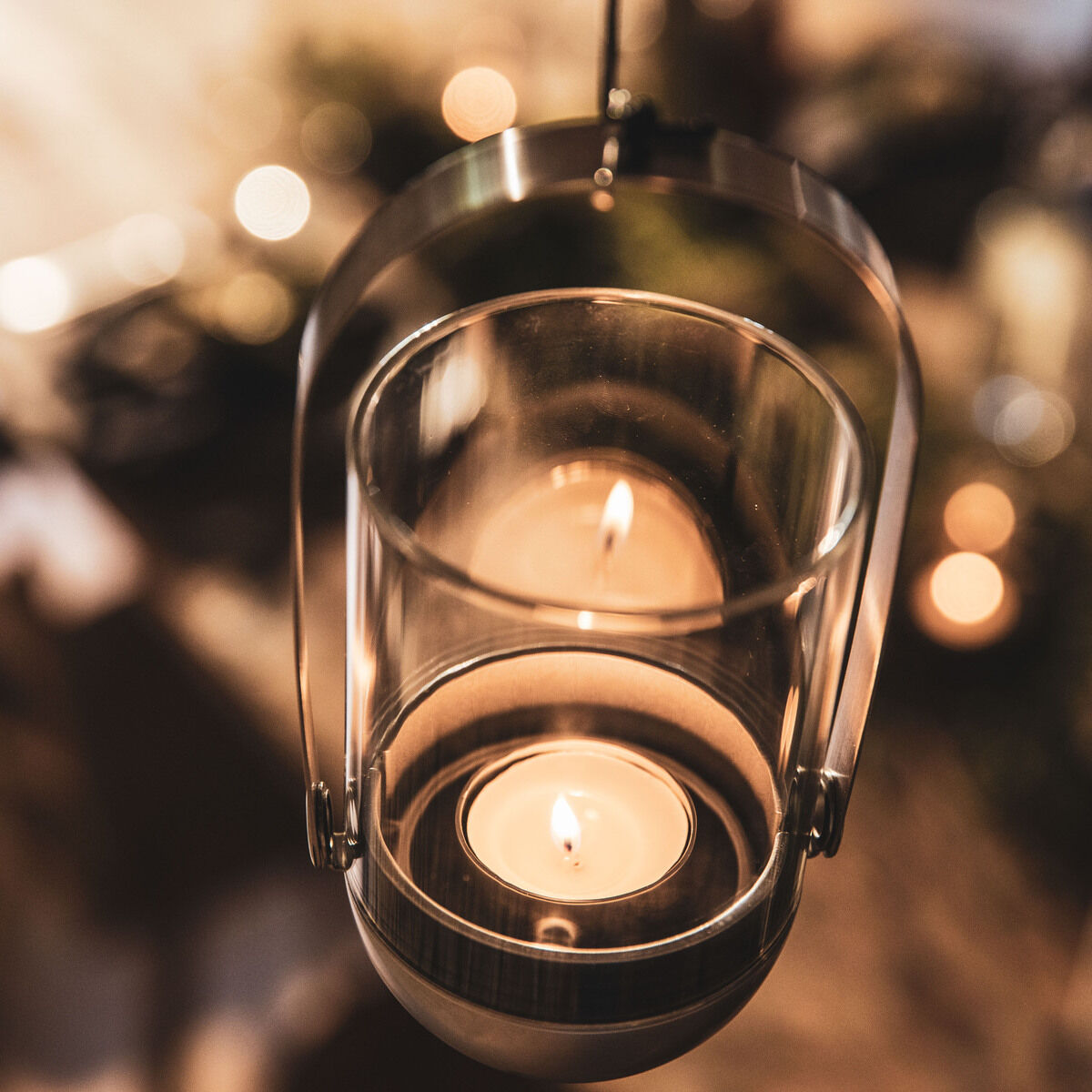 Das Bild zeigt eine Gravity Candle im Hängesystem. Ein Teelicht brennt im Inneren eines Glasbehälters, der in einem metallischen Rahmen aufgehängt ist. Die Szene strahlt eine warme und behagliche Atmosphäre aus.