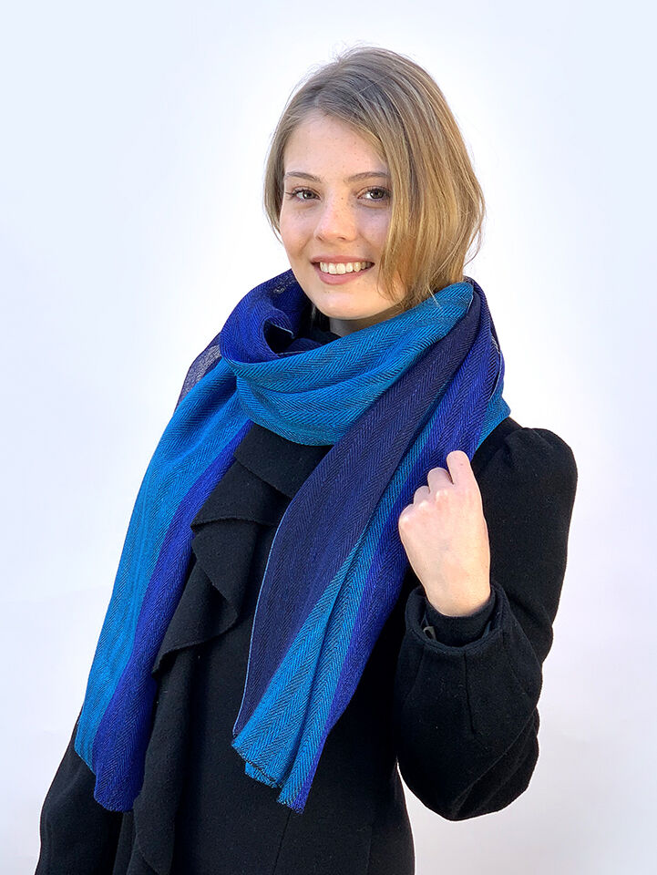Frau trägt einen breiten Schal aus blauem Leinen, kombiniert mit einem schwarzen Mantel.