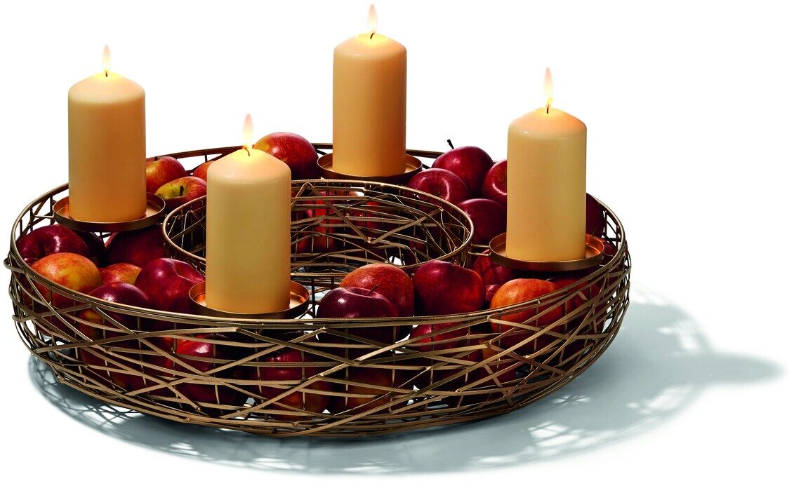 Ein stilvoller Adventskranz mit dem Namen 'Tahoma', bestehend aus einem geflochtenen Holzkörbchen mit vier beige-gelben Kerzen und roten Äpfeln, auf einem weißen Hintergrund. Die Kerzen sind angezündet, was eine warme und gemütliche Atmosphäre schafft.
