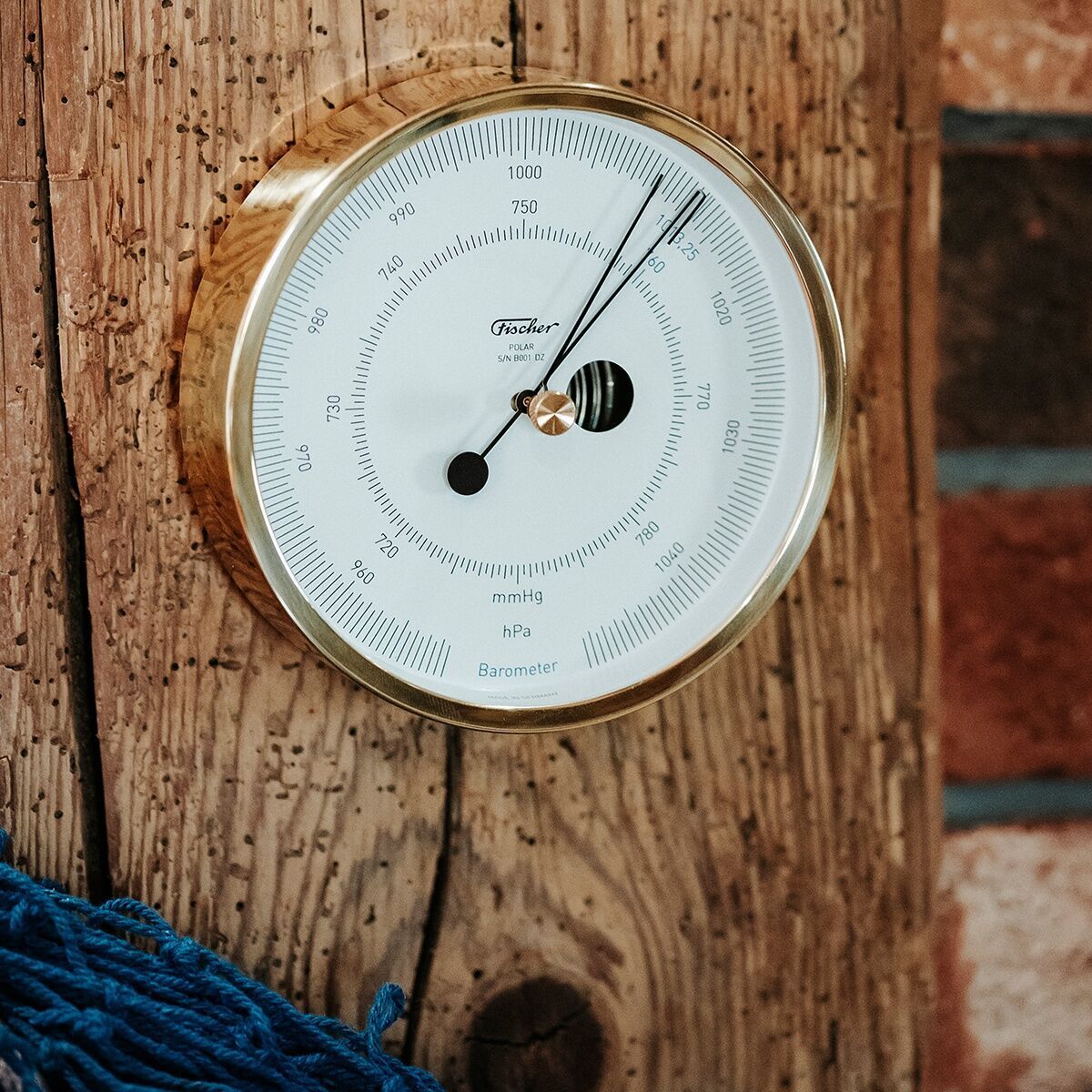 Ein ZEIT-Sonderedition Barometer namens »POLAR«, montiert an einer rustikalen Holzwand. Das präzise Wetterinstrument besitzt ein weißes Zifferblatt mit schwarzen Markierungen und einen goldenen Rahmen.