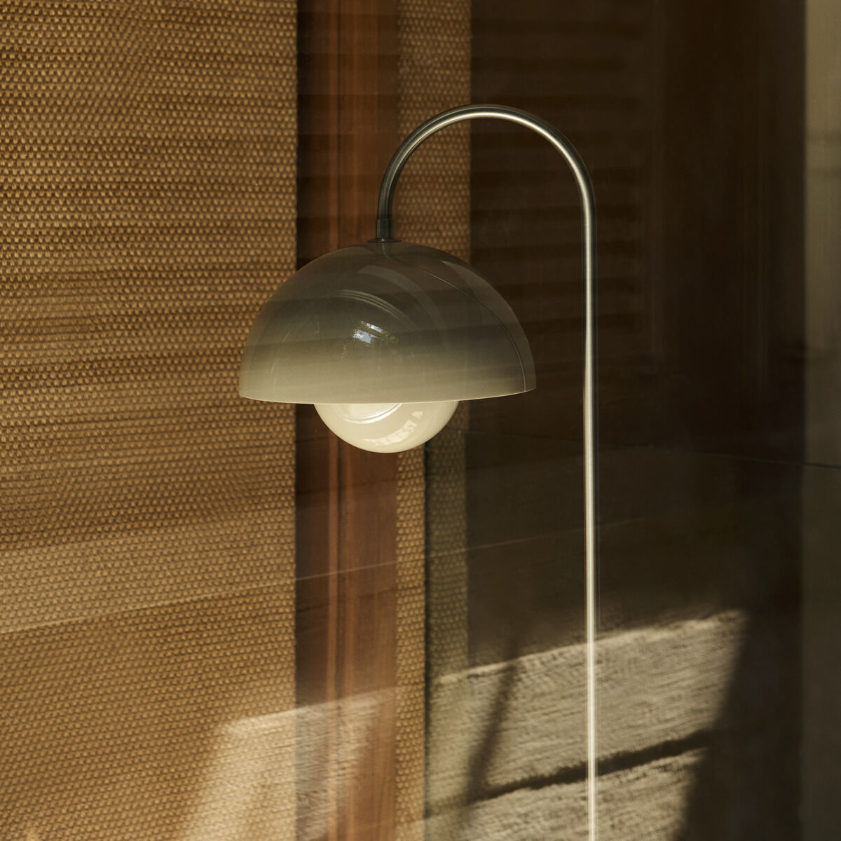 Eine elegante Designerlampe mit einem geschwungenen Ständer und einem halbkugelförmigen Lampenschirm. Das Design wirkt minimalistisch und skandinavisch, passend zu modernen Innenräumen.