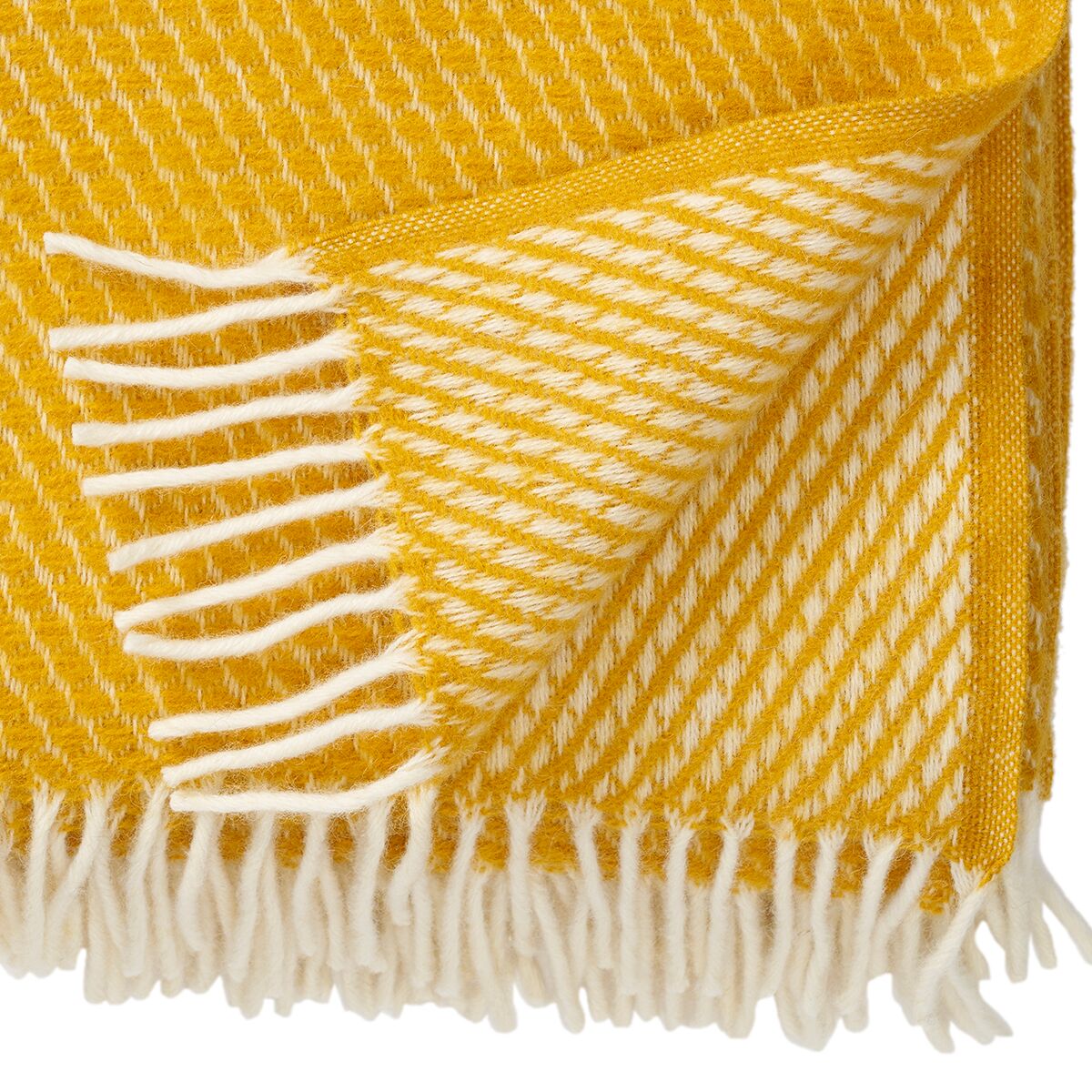 Detailaufnahme einer gelben Kuscheldecke mit Fransen und einem gewebten Muster. Die Decke liegt locker gefaltet, das Material wirkt weich und gemütlich.