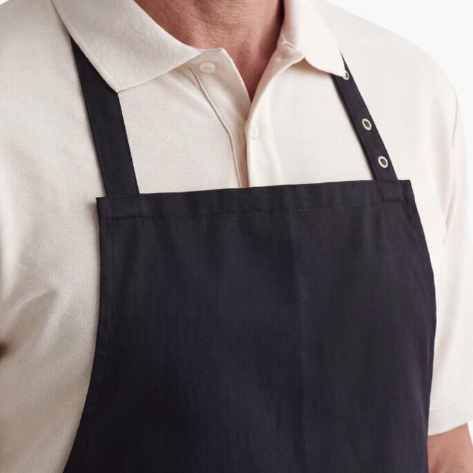 Mann mit beigefarbenem Poloshirt trägt eine schwarze Schürze von Zeitverlag, Produkt Wolfram Siebecks Weihnachtsmenüs Schürze. Der Hintergrund ist weiß, das Bild wirkt puristisch und auf das Produkt fokussiert.