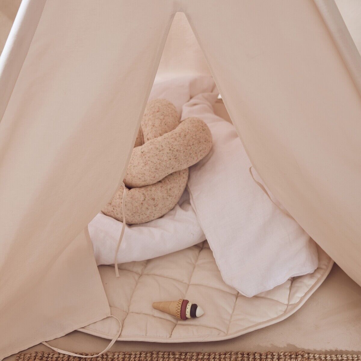 Helles Tipizelt für Kinder mit weicher Bodenmatte, einem Kuschelkissen und einem kleinen Stoffspielzeug auf einem Naturteppich. Das Zelt und das Zubehör sind in sanften Naturfarben gehalten und schaffen eine gemütliche Spielecke.
