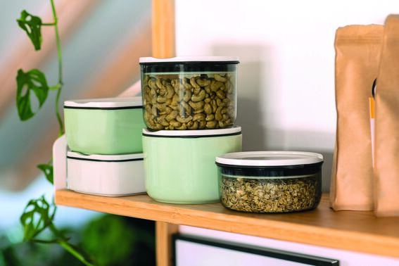 Mehrere Lunchboxen in der Farbe »mineral« stehen auf einem hölzernen Regal. Die Boxen haben transparente Deckel mit schwarzem Rand und sind gefüllt mit verschiedenen Lebensmitteln.