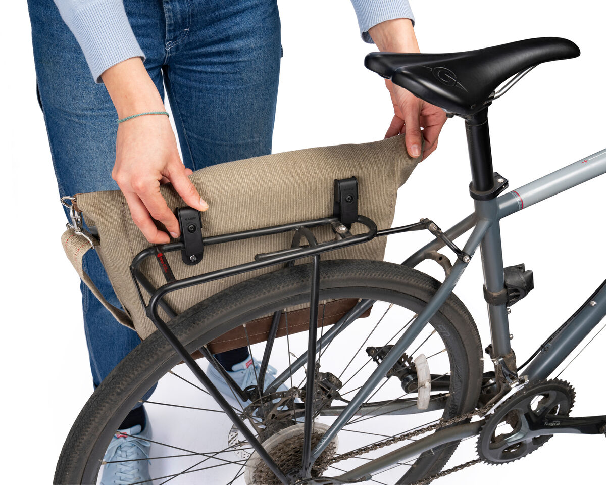 Eine Person befestigt eine beige Fahrradtasche an einem silbernen Fahrradgepäckträger.