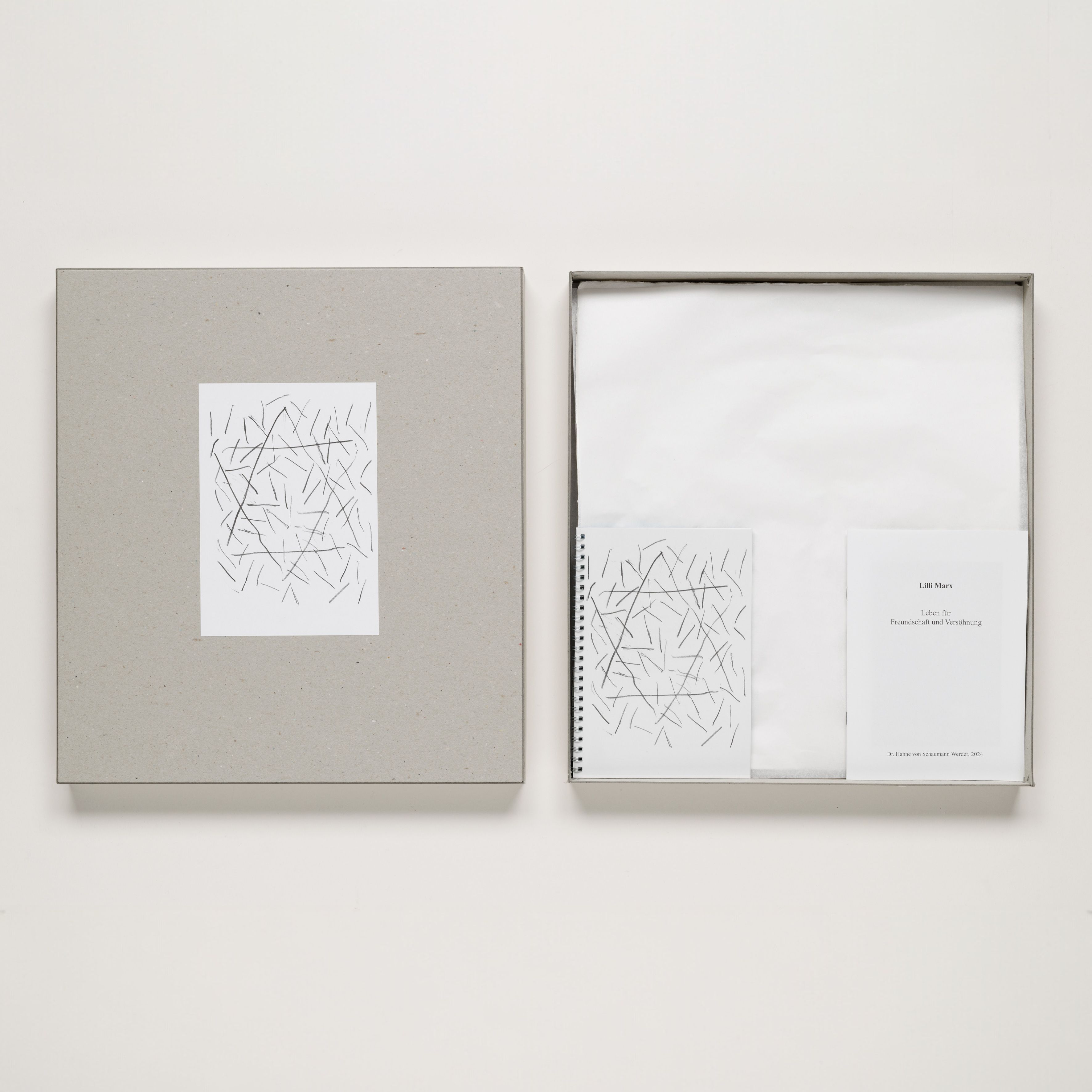 Ein geöffneter Karton mit Günther Uecker Prägedrucken, darunter ein Buch mit einem abstrakten Kunstwerk in Schwarz-Weiß und Begleitmaterialien für das Lilli Marx Haus in Düsseldorf.