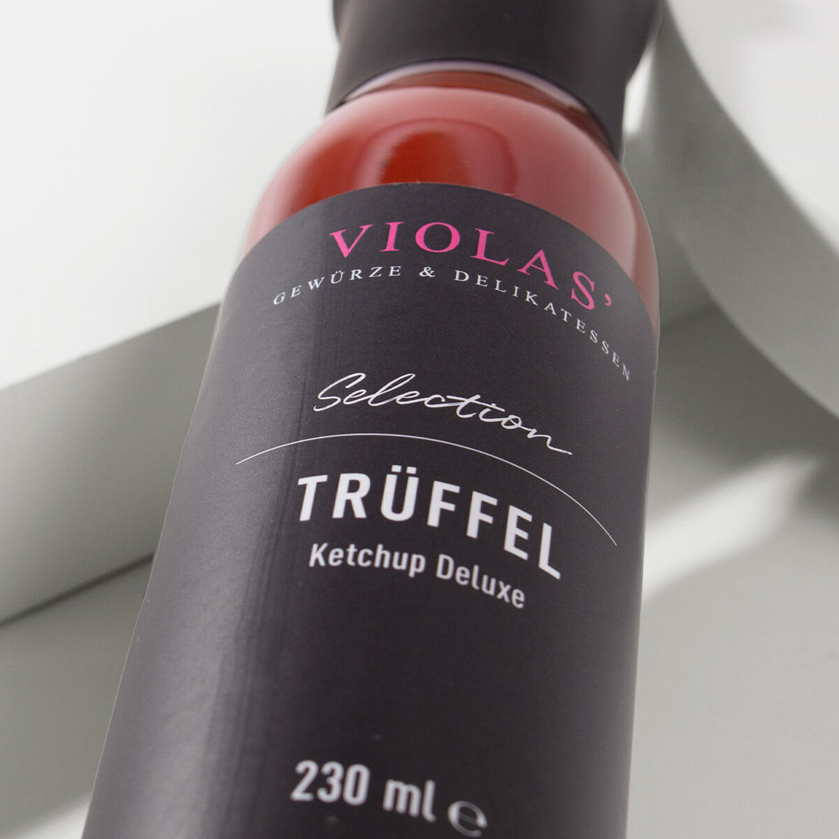 Eine Flasche 'VIOLAS' Ketchup Deluxe Trüffel mit schwarzem Etikett und rotem Inhalt, 230 ml, auf hellem Hintergrund.