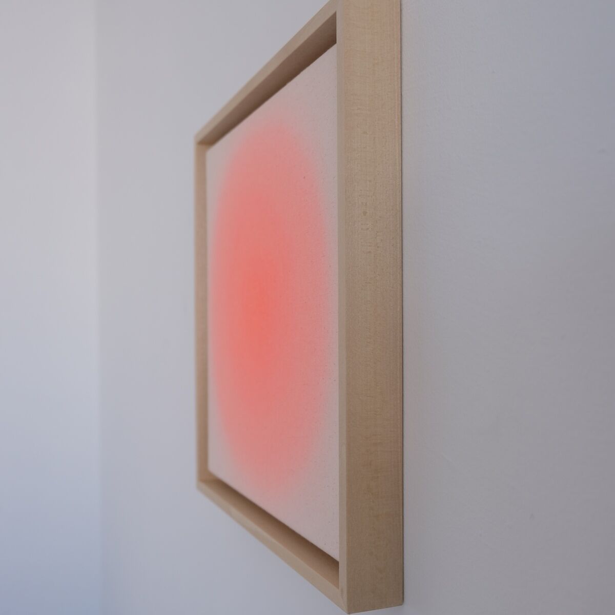 Das Bild zeigt ein quadratisches Kunstwerk in Apricot-Tönen, das an einer weißen Wand hängt. Die Leinwand besitzt einen sanften Farbverlauf in der Mitte und ist von einem schlichten, hellen Holzrahmen eingefasst. Das abstrakte Motiv erzeugt einen ruhigen, modernen Eindruck.