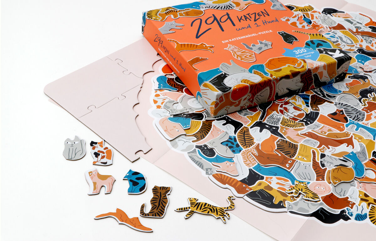Ein Puzzle mit dem Titel »299 Katzen«, das verschiedene bunte Katzenmotive zeigt. Die Puzzleteile und die Verpackung sind auf einem weißen Hintergrund abgebildet. Einige Katzenpuzzleteile liegen außerhalb der Verpackung.