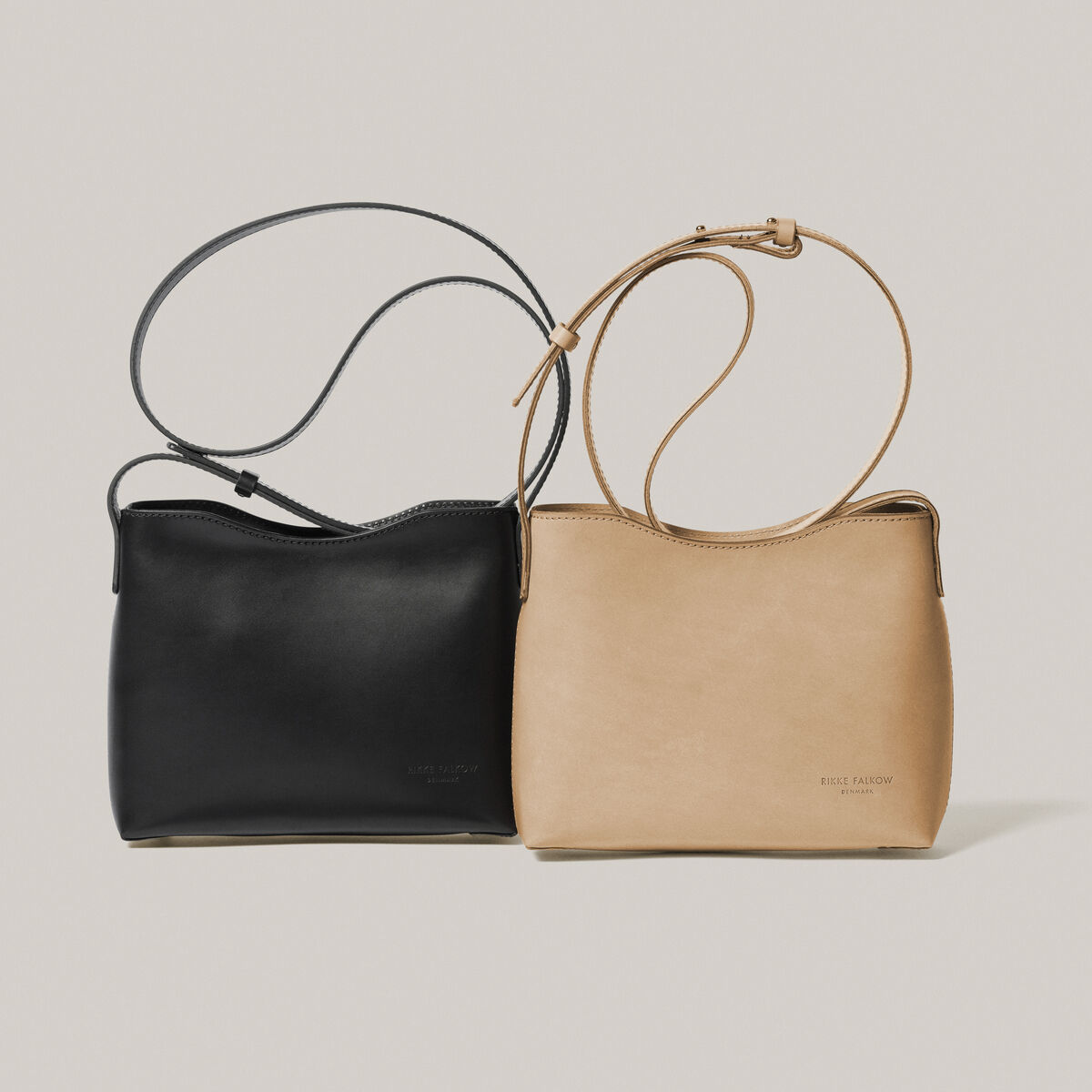 Zwei Schultertaschen aus Kernleder, eine in Schwarz und eine in Beige, vor einem hellen Hintergrund.