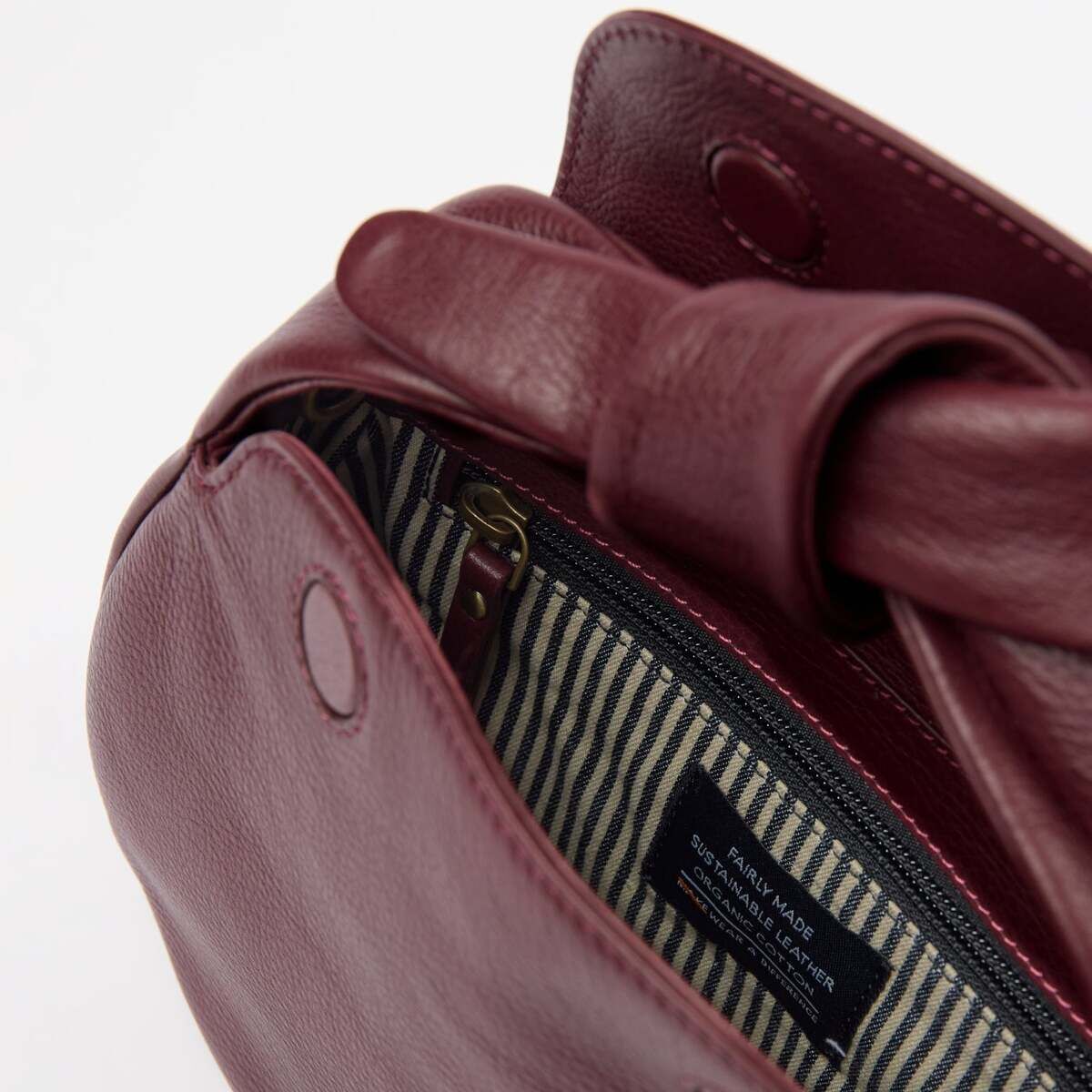 Detailansicht einer bordeauxroten Umhängetasche in Lederoptik mit gestreiftem Innenfutter und Reißverschluss, geeignet für Damen und modebewusste Personen.