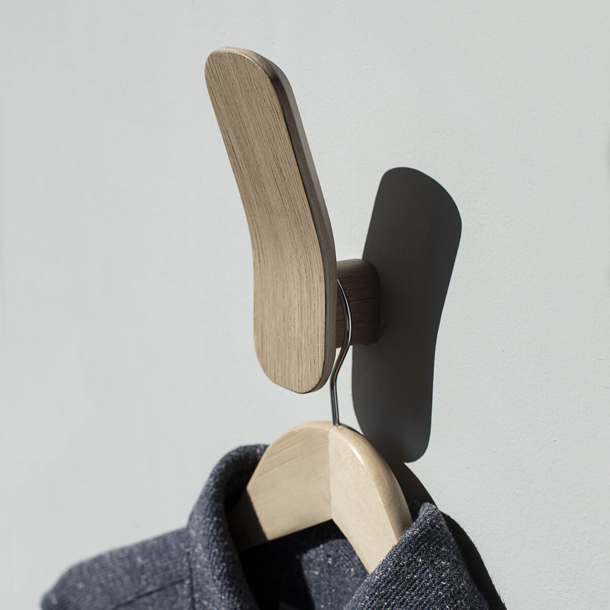 Ein moderner Kleiderhaken aus Eiche-Holz mit einem minimalistischen Design. An der Wand befestigt, hängt ein graues Kleidungsstück an einem Holzbügel.