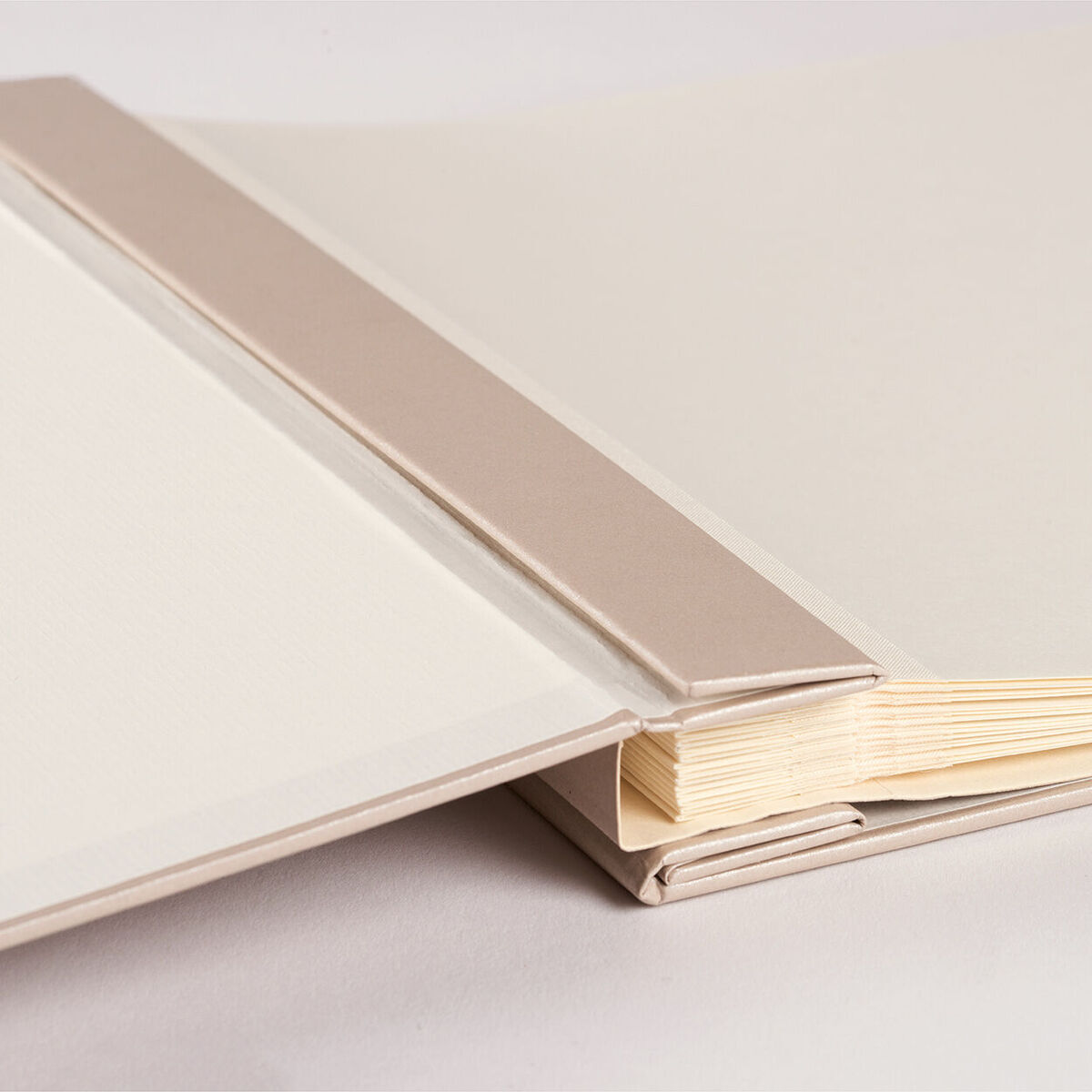 Ein schlichtes Fotoalbum in Beige und Weiß mit einem hellbraunen Buchrücken liegt auf einem neutralen Untergrund.