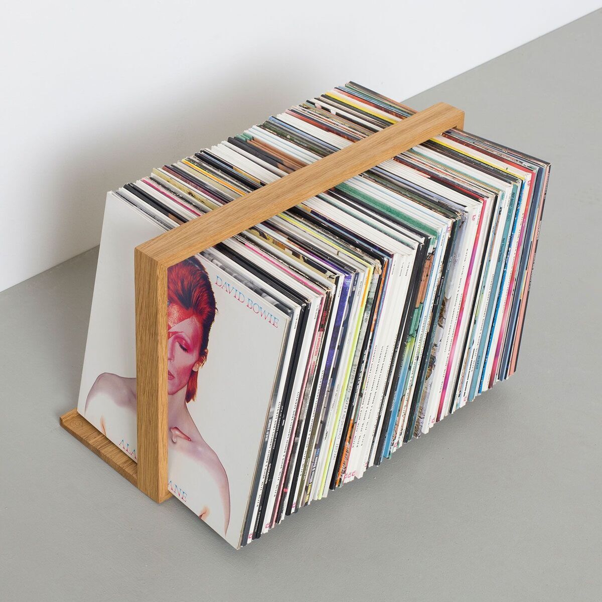 Ein moderner Plattenständer aus Holz, gefüllt mit einer Sammlung von Schallplatten. Der Ständer hat ein einfaches, minimalistisches Design und zeigt die Cover der Schallplatten an der Vorderseite.