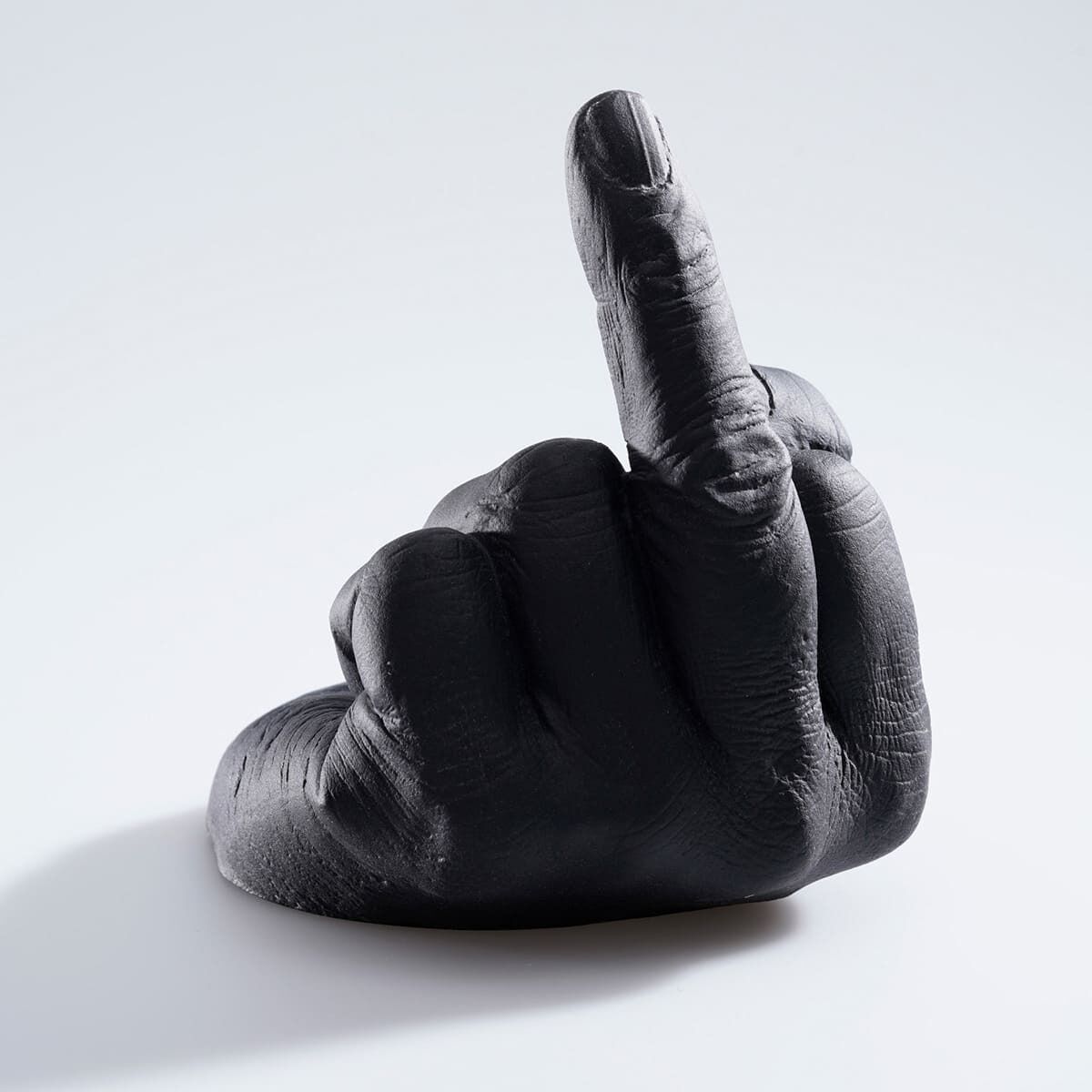 Eine Skulptur von Ai Weiwei, »Study of Perspective in Glass«, die eine Hand zeigt, deren mittlerer Finger aufrechtsteht. Die Skulptur ist in einem dunklen Farbton gehalten und steht auf einer weißen Oberfläche.