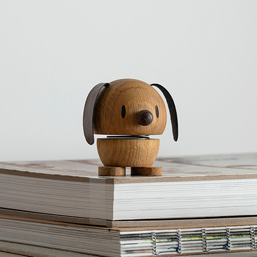 Kleine hölzerne Hundefigur mit abgerundeter Form, schwarzen Ohren und Nase, steht auf einem Stapel Bücher.