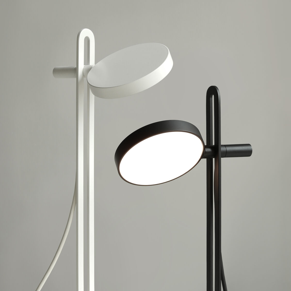 Zwei moderne Tischlampen der Serie „Echo“ in schwarzer und weißer Farbe stehen vor einem grauen Hintergrund. Die Lampen besitzen ein minimalistisches, zeitgenössisches Design mit schlanken Ständern und rundem Lampenschirm. Perfekt für den Einsatz im Büro oder Wohnbereich.