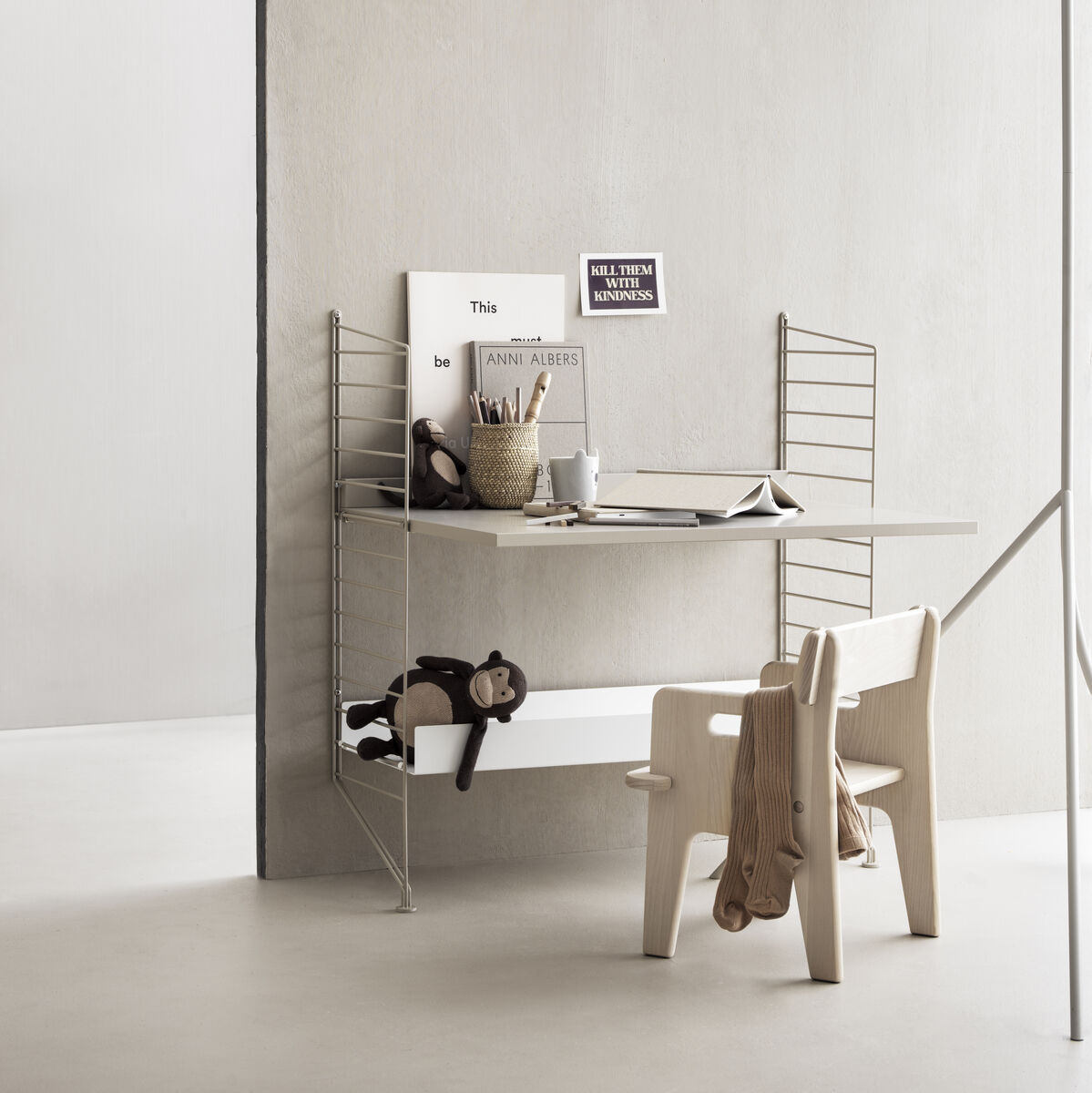 Ein stilvoller Kinderzimmer-Schreibtisch mit einem Schreibtischstuhl und Spielzeug. Der Schreibtisch ist mit Büchern, Farben und Schreibutensilien ausgestattet und steht vor einer beige Wand. Die Umgebung ist minimalistisch und funktional gestaltet, ideal für das Lernen und kreative Aktivitäten von Kindern.