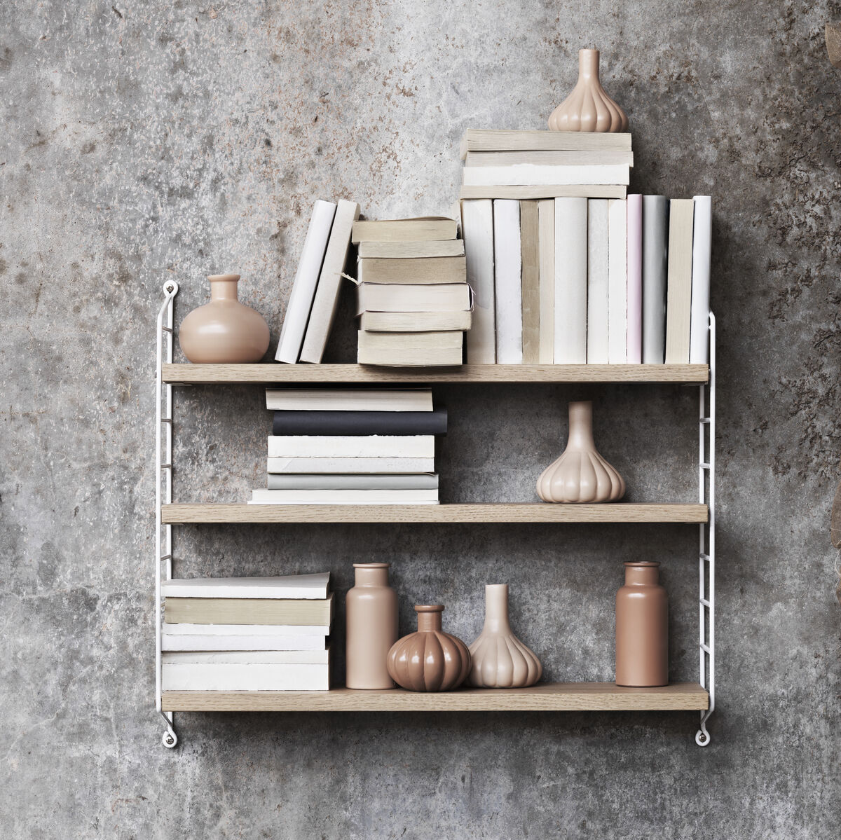Ein minimalistisches Wandregal-System aus Holz und Metall, dekoriert mit Büchern und Vasen vor einer strukturierten grauen Wand.