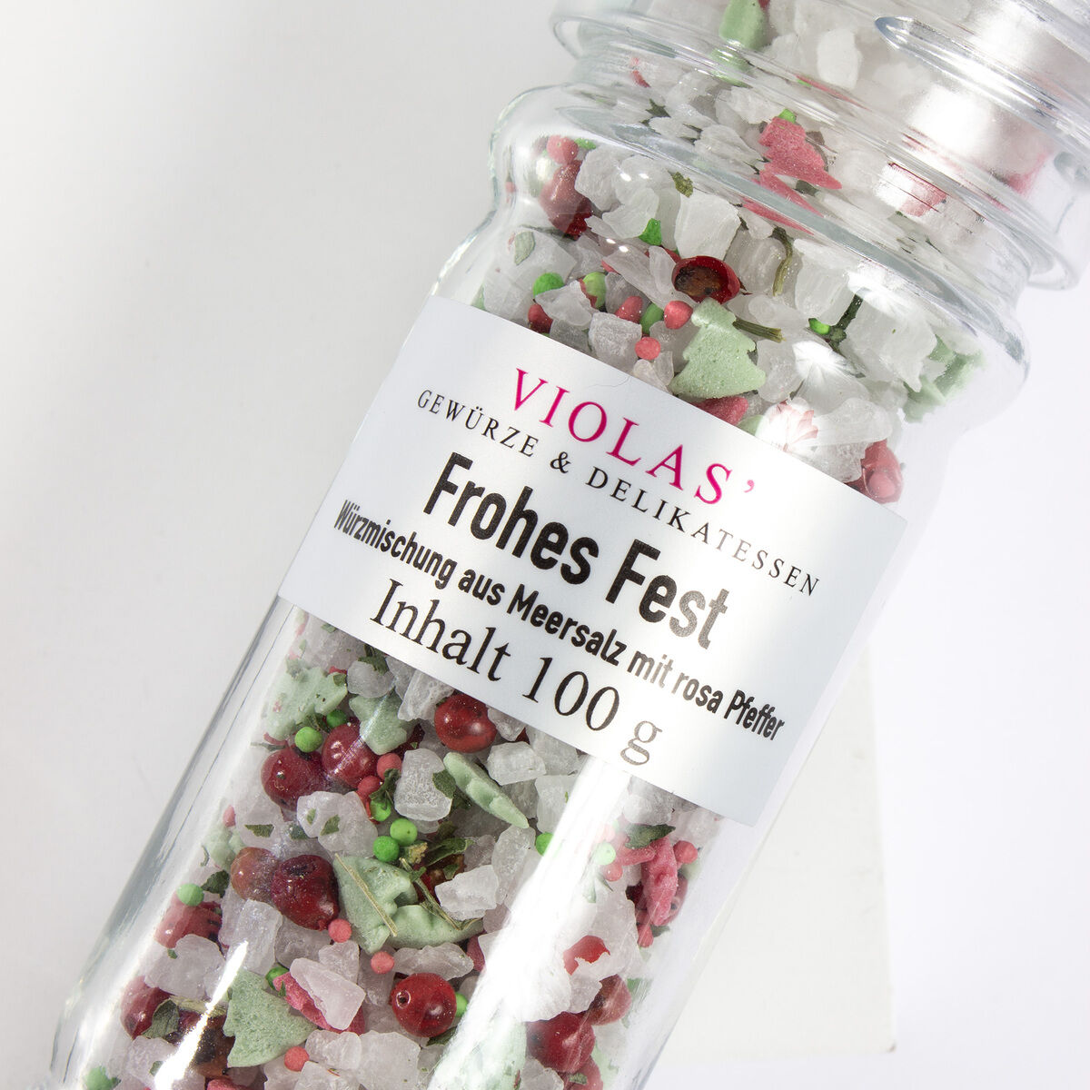 Geschenkset mit dem Titel 'Frohes Fest' von VIOLAS' im Glasbehälter, gefüllt mit einer Mischung aus grobem Meersalz und rosa Pfeffer. Das Produkt ist weihnachtlich dekoriert in überwiegend weißen, pinken, roten und grünen Farben.