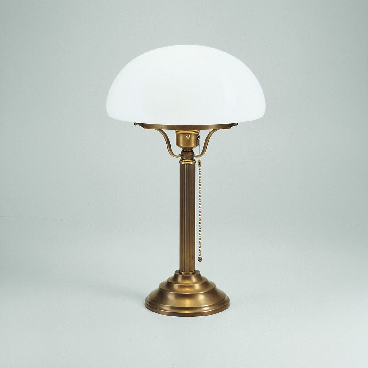 Elegante Jugendstil-Pilzleuchte »Berlin« von Ars mundi aus Berliner Messing mit rundem Standfuß und Kettenschalter. Der Schirm aus mundgeblasenem, weißem Opalglas bildet einen Kontrast zum gold-bronzefarbenen Gestell. Zeitloses Design für stilvolle Räume.