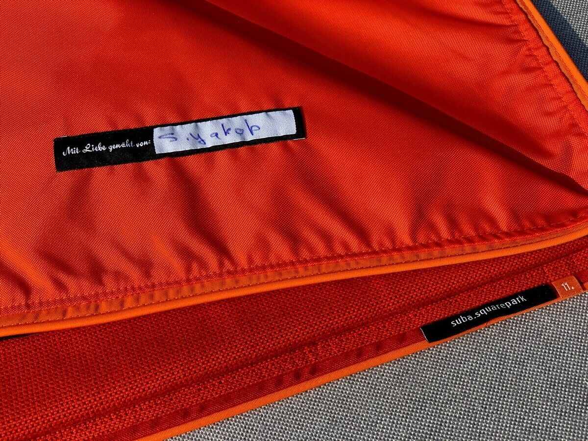 Orange Picknickdecke mit grauer Unterseite und Etiketten, die auf einem Outdoor-Untergrund liegen.